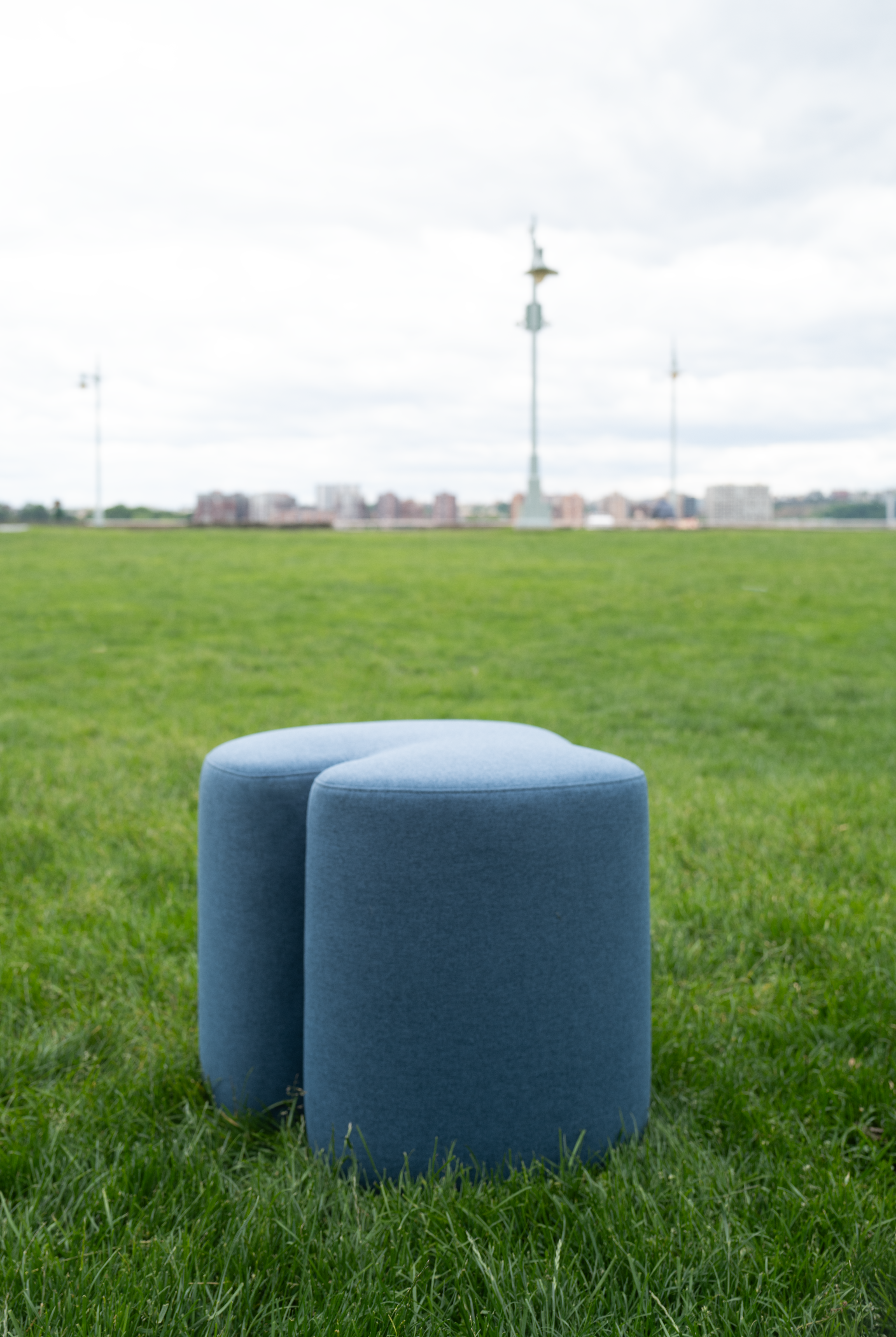 Two blue cylindrical ottomans on grass with a distant cityscape.