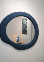 Round blue mirror on a white wall with a painting in the reflection