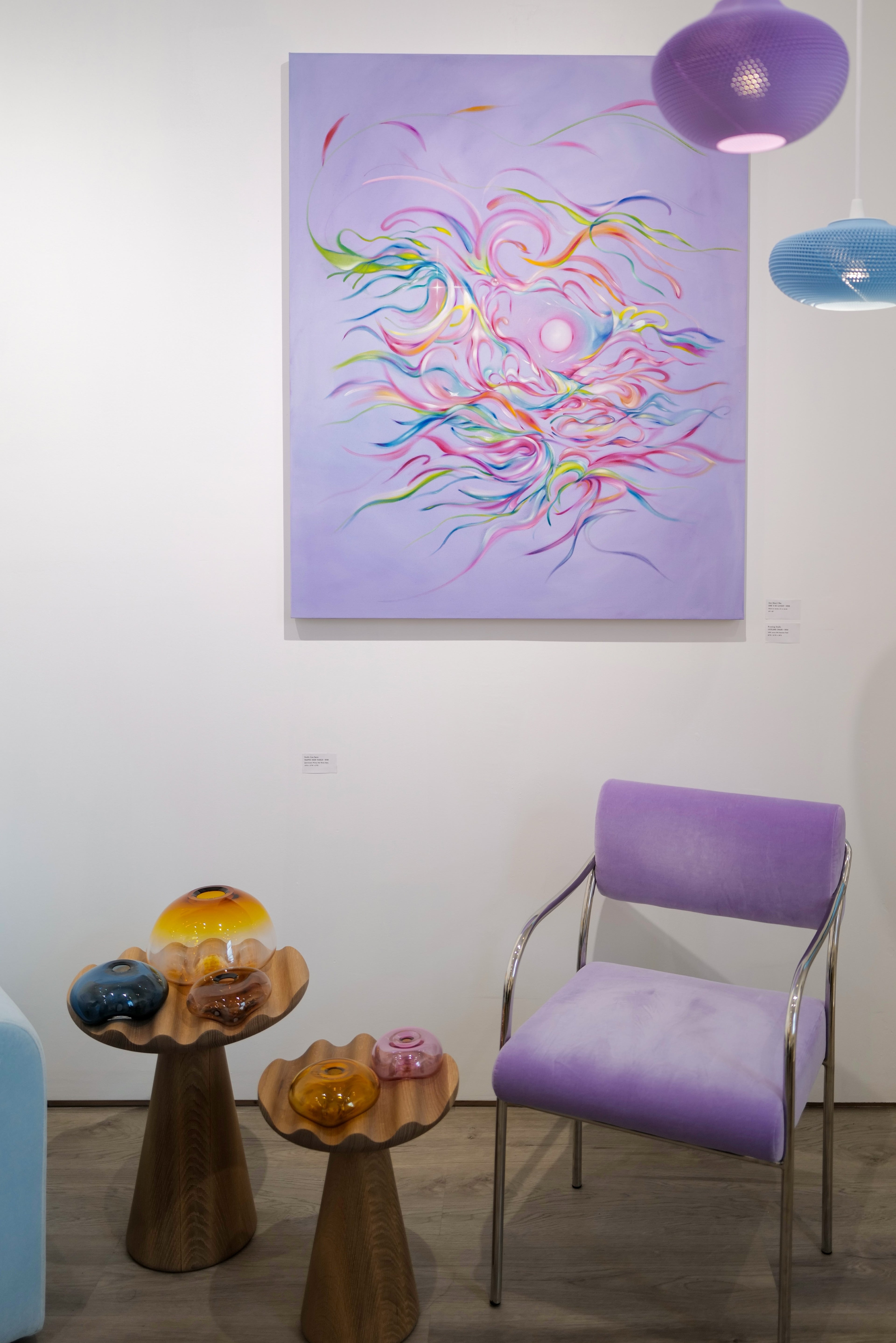 Colorful abstract painting on a white wall above a purple chair and small wooden table.