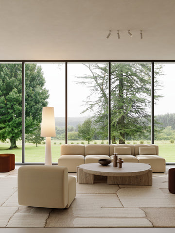 Modern living room with large windows, beige sofa, and round coffee table.